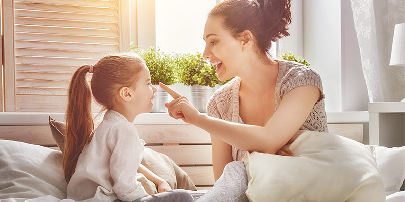 A mother playing with her daughter in front of a bedroom window.